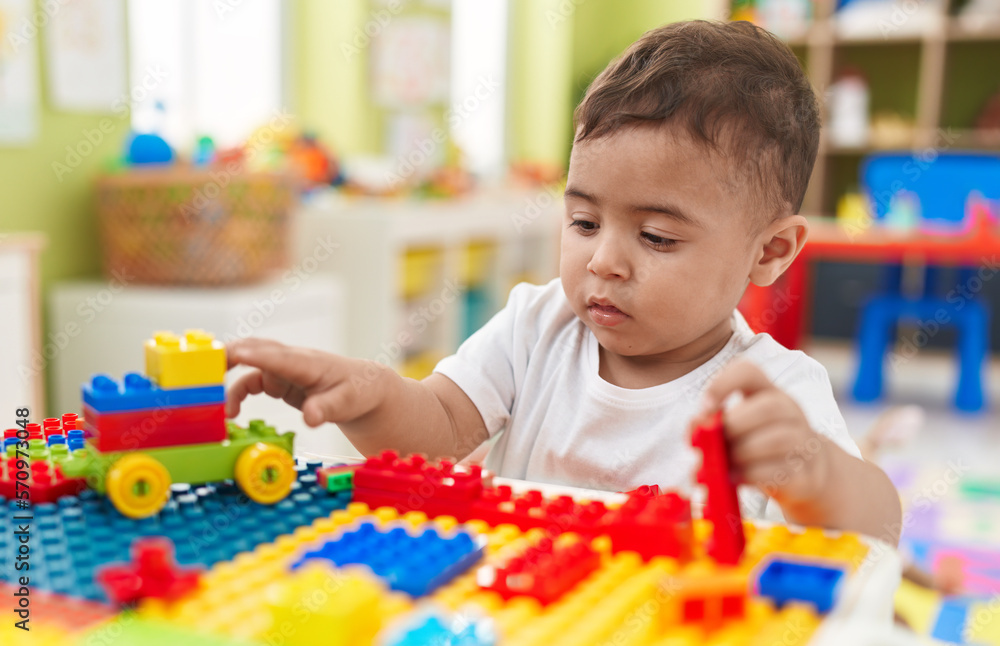 Adorable hispanic toddler playing with construction blocks sitting on table at kindergarten Adorable hispanic toddler playing with construction blocks sitting on table at kindergarten
