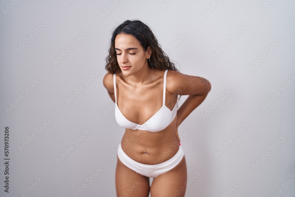 Fototapeta premium Young hispanic woman wearing white lingerie suffering of backache, touching back with hand, muscular pain
