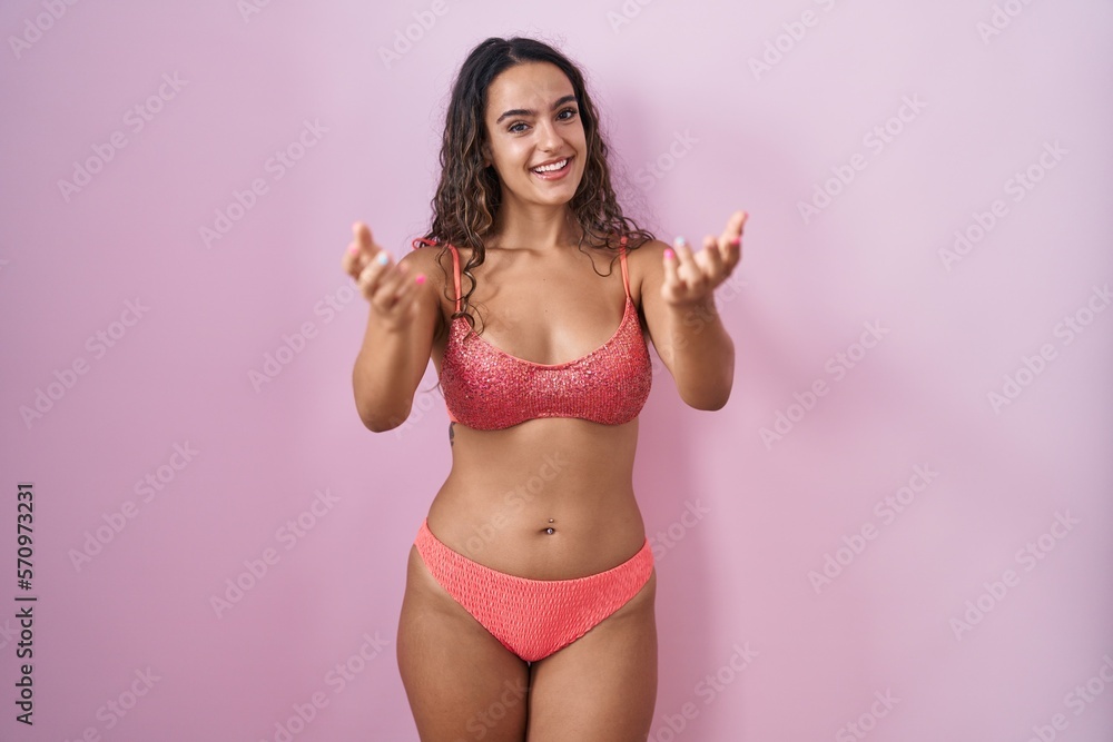 Young hispanic woman wearing lingerie over pink background smiling cheerful offering hands giving assistance and acceptance. Young hispanic woman wearing lingerie over pink background smiling cheerful offering hands giving assistance and acceptance.