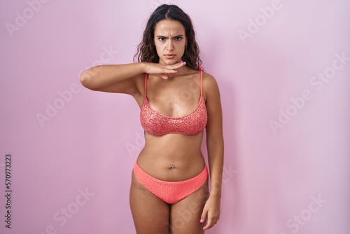 Young hispanic woman wearing lingerie over pink background cutting throat with hand as knife, threaten aggression with furious violence