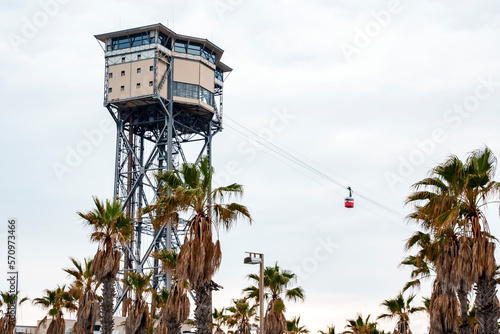 Low angle view of Torre Sant Sebastia a aerial tramway with cable car and restaurant on top of tower and palm trees growing under cloudy sky at Catalonia in Barcelona, Spain photo