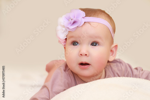 Portrait of a beautiful little girl 6 months old. Close-up of a baby on a bright background in the studio. Beautiful girl with a bow on her hair. Baby care. Children Protection Day.
