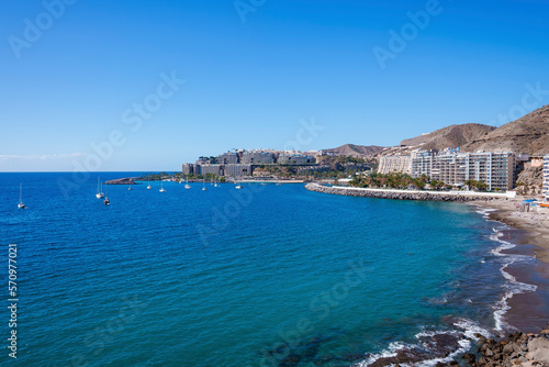Fototapeta Naklejka Na Ścianę i Meble -  Scenic view of beach and ships sailing on beautiful seascape by buildings at coastline. Clear blue sky in the background on a sunny day at Gran Canaria island in Spain