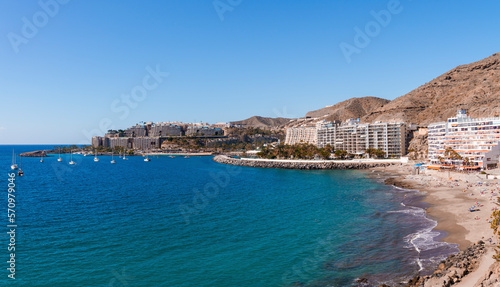 Aerial view of beach and ships sailing on beautiful seascape by buildings at coastline with clear blue sky in the background. A sunny day at Gran Canaria island in Spain