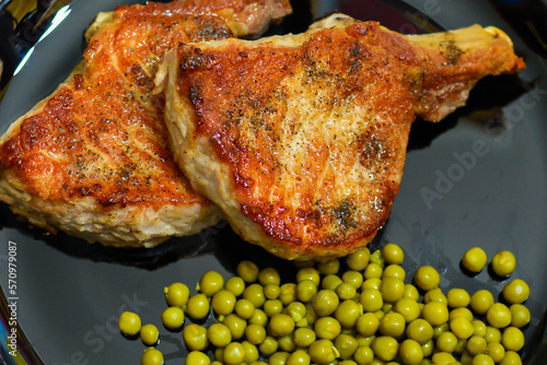Steak on the bone from pork with green peas in a plate