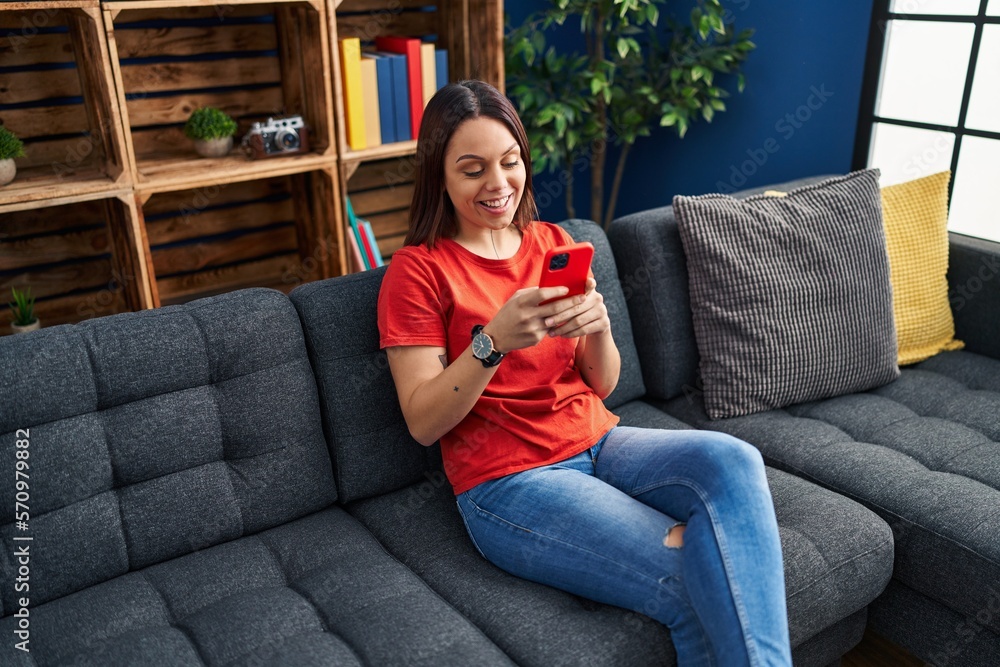 Young beautiful hispanic woman using smartphone sitting on sofa at home Young beautiful hispanic woman using smartphone sitting on sofa at home