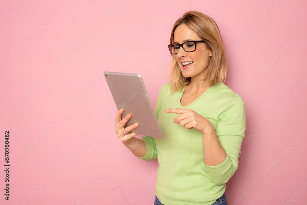 Young smiling woman using tablet standing isolated over pink background. Young smiling woman using tablet standing isolated over pink background.