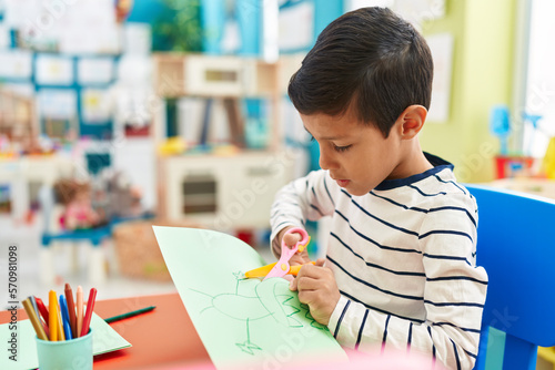 Adorable hispanic boy student cutting paper at kindergarten photo