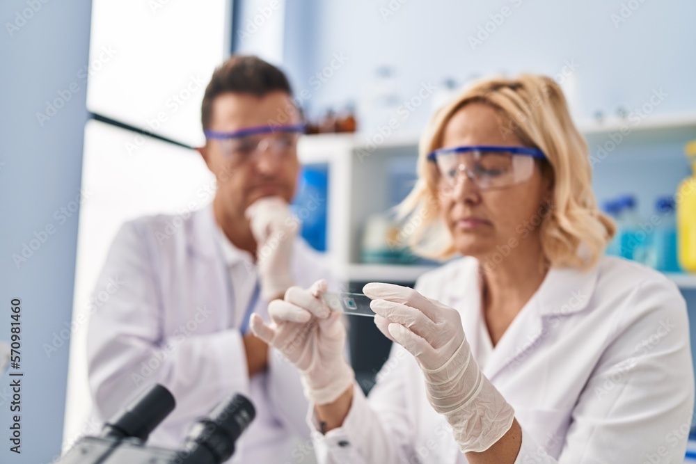 Middle age man and woman scientist partners holding sample working at laboratory