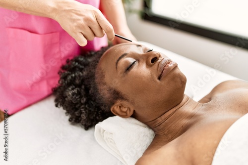 African american woman lying on massage table having eyebrows treatment at beauty salon