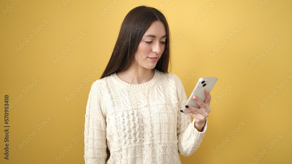 Young beautiful hispanic woman using smartphone with serious expression over isolated yellow background Young beautiful hispanic woman using smartphone with serious expression over isolated yellow background