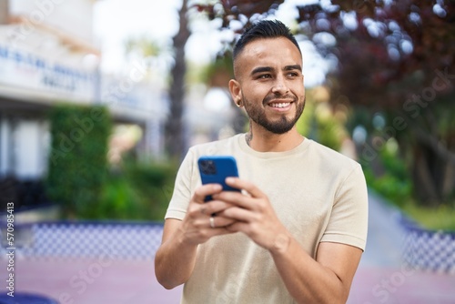 Young hispanic man smiling confident using smartphone at park © Krakenimages.com