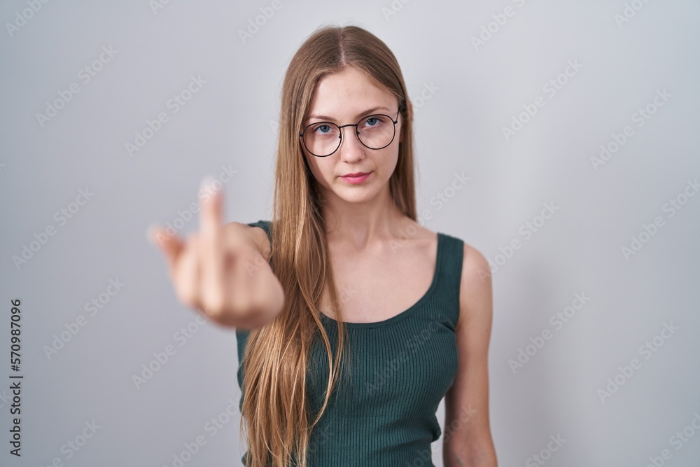 Young caucasian woman standing over white background showing middle finger, impolite and rude fuck off expression Young caucasian woman standing over white background showing middle finger, impolite and rude fuck off expression