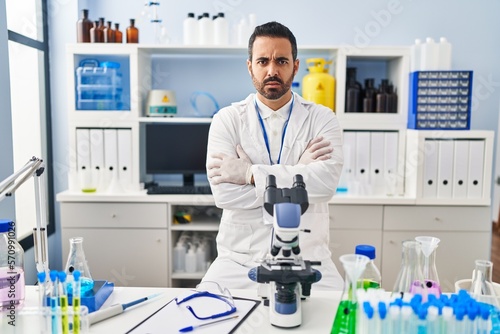 Young hispanic man with beard working at scientist laboratory skeptic and nervous  disapproving expression on face with crossed arms. negative person.