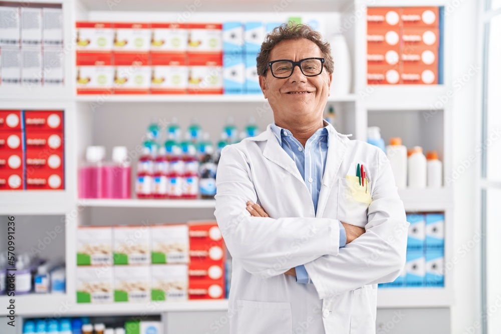 Middle age man pharmacist smiling confident standing with arms crossed gesture at pharmacy