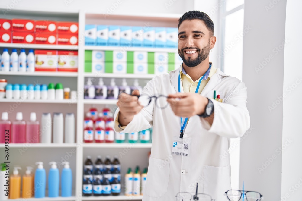 Young arab man pharmacist smiling confident holding glasses at pharmacy