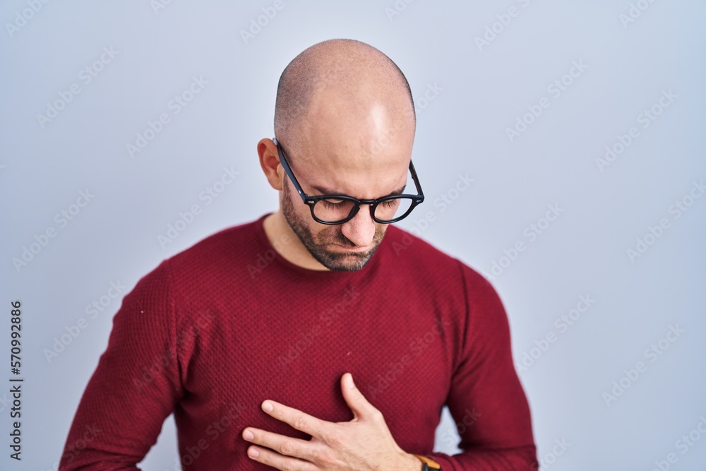 Naklejka premium Young bald man with beard standing over white background wearing glasses with hand on stomach because indigestion, painful illness feeling unwell. ache concept.