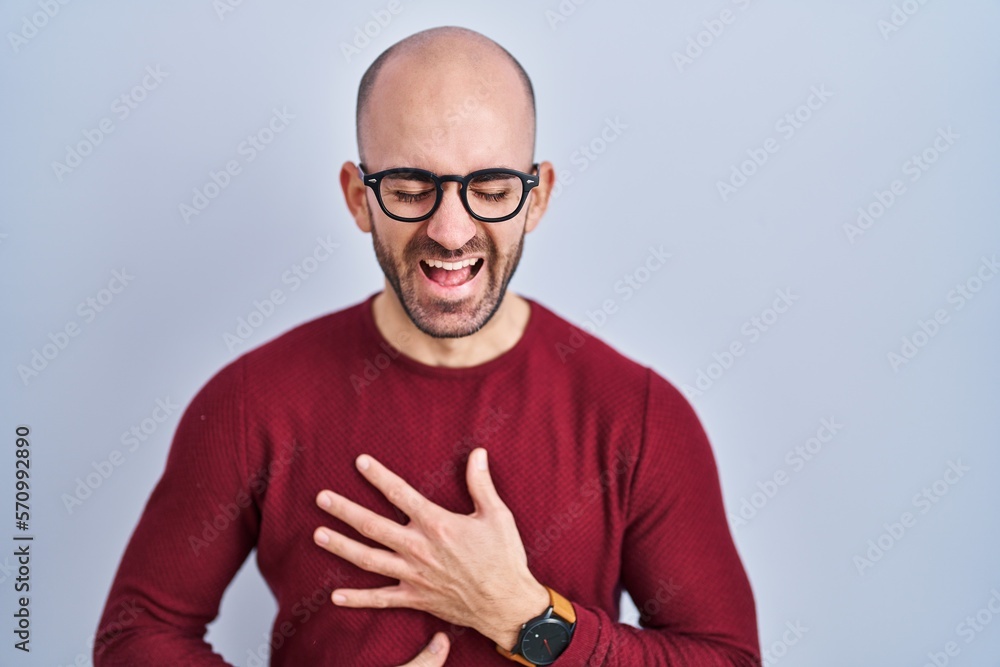 Young bald man with beard standing over white background wearing glasses smiling and laughing hard out loud because funny crazy joke with hands on body. Young bald man with beard standing over white background wearing glasses smiling and laughing hard out loud because funny crazy joke with hands on body.