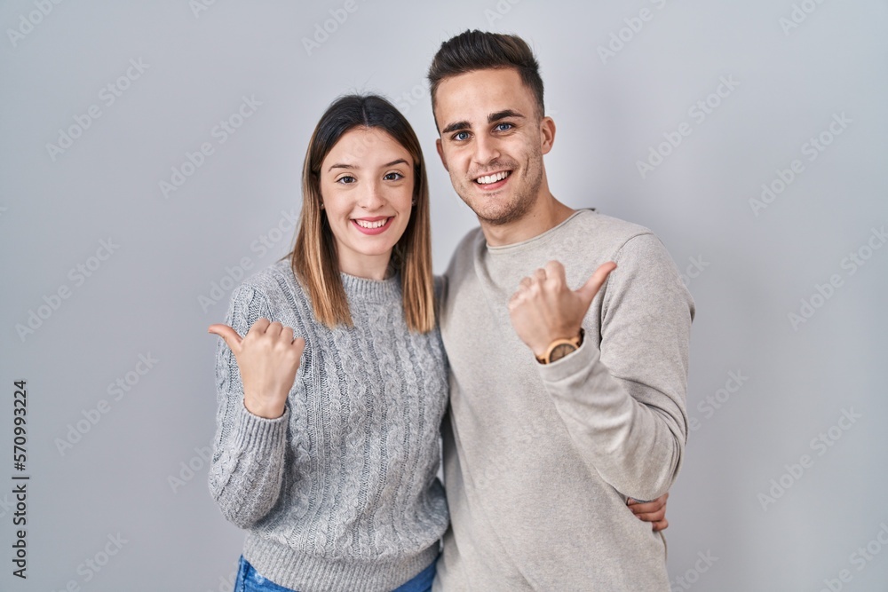 Young hispanic couple standing over white background pointing to the back behind with hand and thumbs up, smiling confident Young hispanic couple standing over white background pointing to the back behind with hand and thumbs up, smiling confident