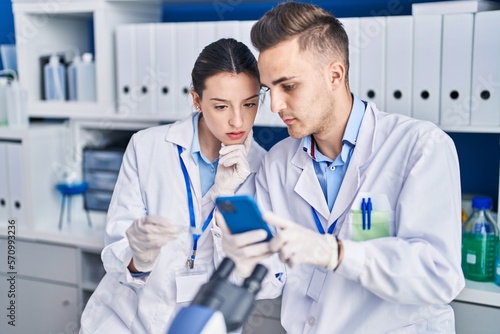 Man and woman scientists using smartphone looking sample at laboratory