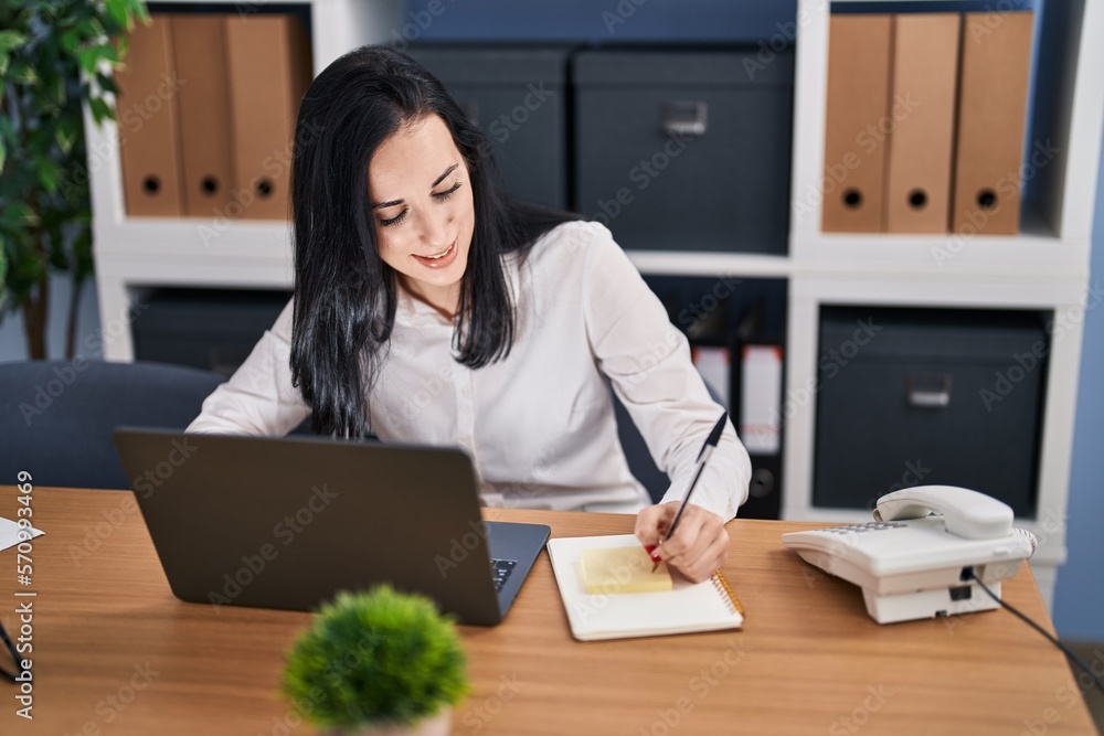 Young caucasian woman business worker using laptop writing on reminder paper at office Young caucasian woman business worker using laptop writing on reminder paper at office