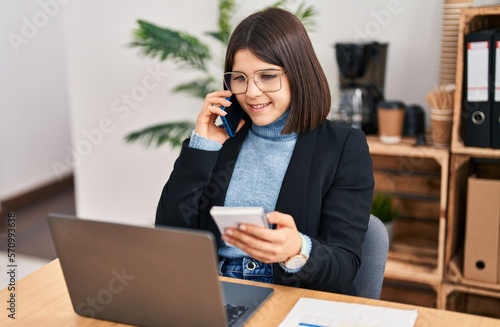 Young beautiful hispanic woman business worker talking on smartphone reading notebook at office