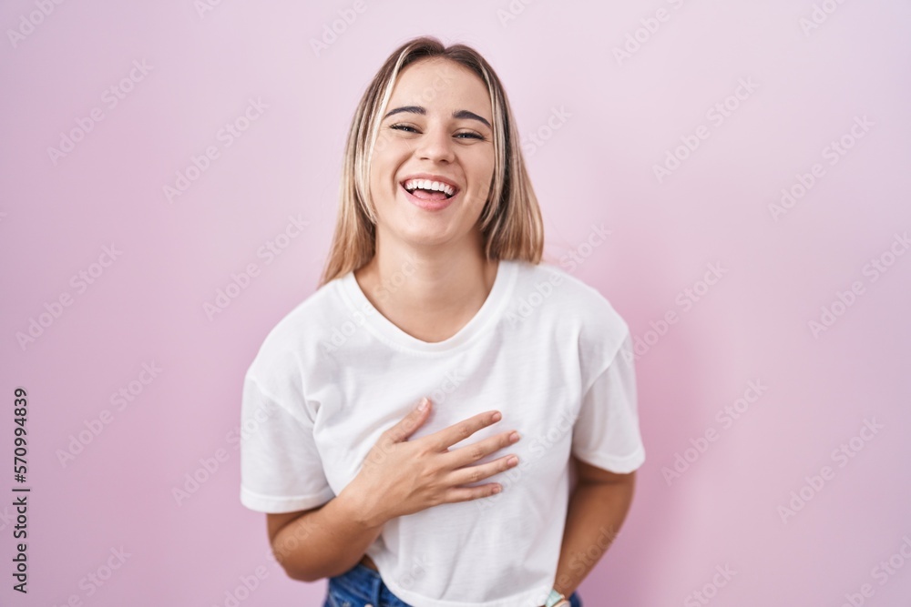 Young blonde woman standing over pink background smiling and laughing hard out loud because funny crazy joke with hands on body. Young blonde woman standing over pink background smiling and laughing hard out loud because funny crazy joke with hands on body.