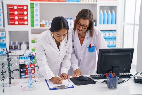 Two women pharmacist smiling confident writing on document at pharmacy