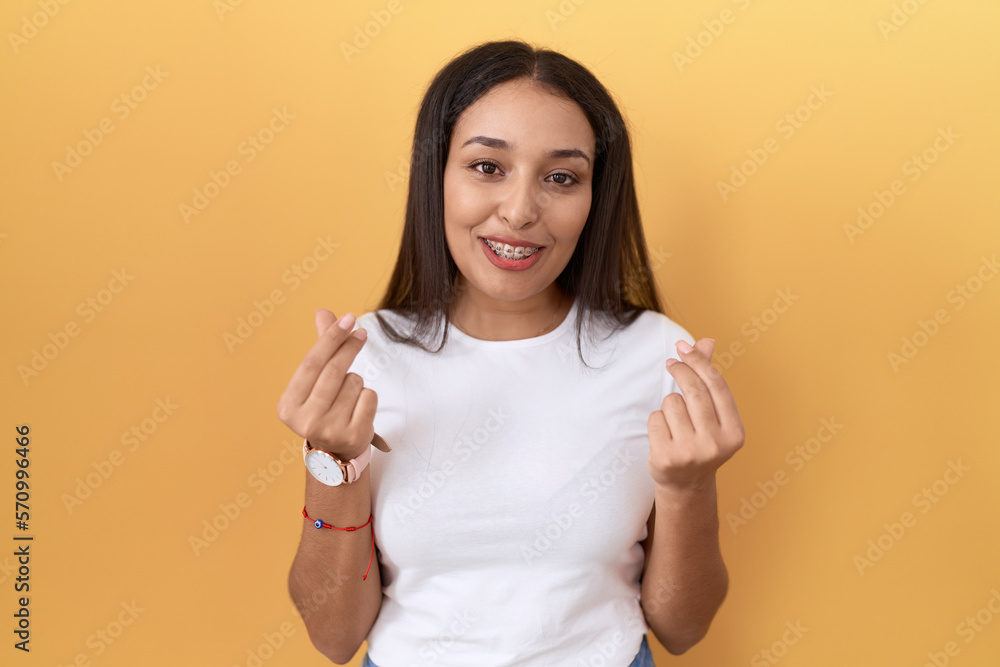Young arab woman wearing casual white t shirt over yellow background doing money gesture with hands, asking for salary payment, millionaire business Young arab woman wearing casual white t shirt over yellow background doing money gesture with hands, asking for salary payment, millionaire business