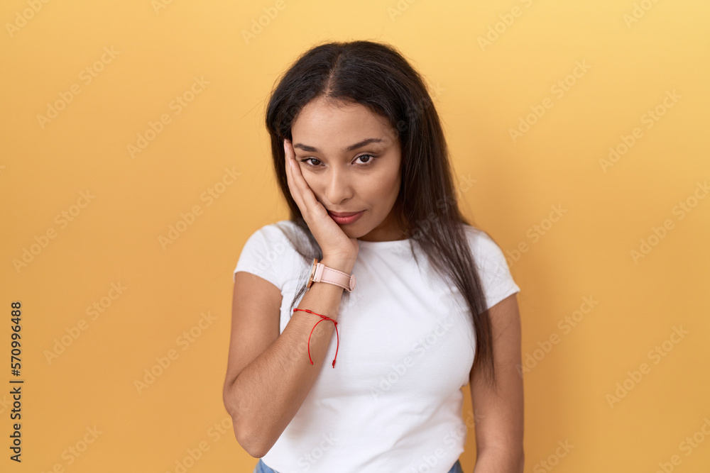 Young arab woman wearing casual white t shirt over yellow background thinking looking tired and bored with depression problems with crossed arms. Young arab woman wearing casual white t shirt over yellow background thinking looking tired and bored with depression problems with crossed arms.