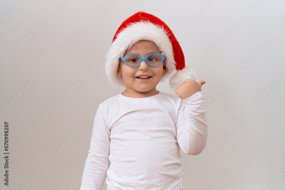 Little hispanic boy wearing glasses and christmas hat pointing thumb up to the side smiling happy with open mouth Little hispanic boy wearing glasses and christmas hat pointing thumb up to the side smiling happy with open mouth