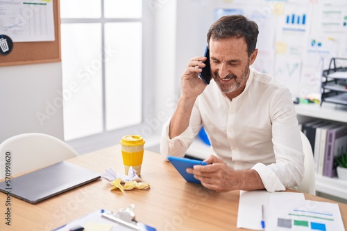 Middle age man business worker talking on smartphone using touchpad at office