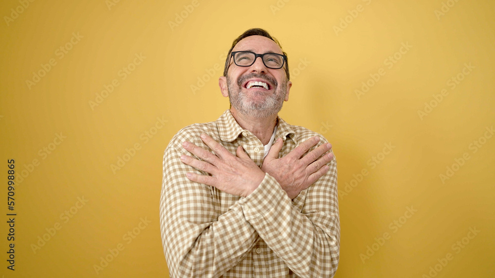 Fototapeta premium Middle age man smiling confident hugging himself over isolated yellow background