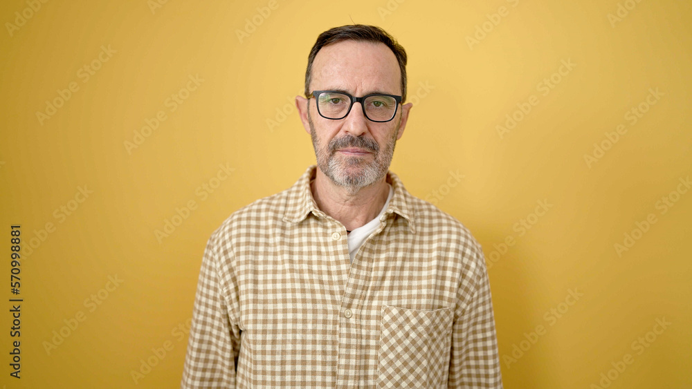 Middle age man wearing glasses with relaxed expression over isolated yellow background Middle age man wearing glasses with relaxed expression over isolated yellow background