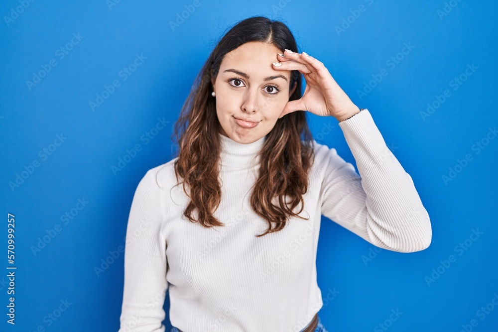 Young hispanic woman standing over blue background worried and stressed about a problem with hand on forehead, nervous and anxious for crisis Young hispanic woman standing over blue background worried and stressed about a problem with hand on forehead, nervous and anxious for crisis
