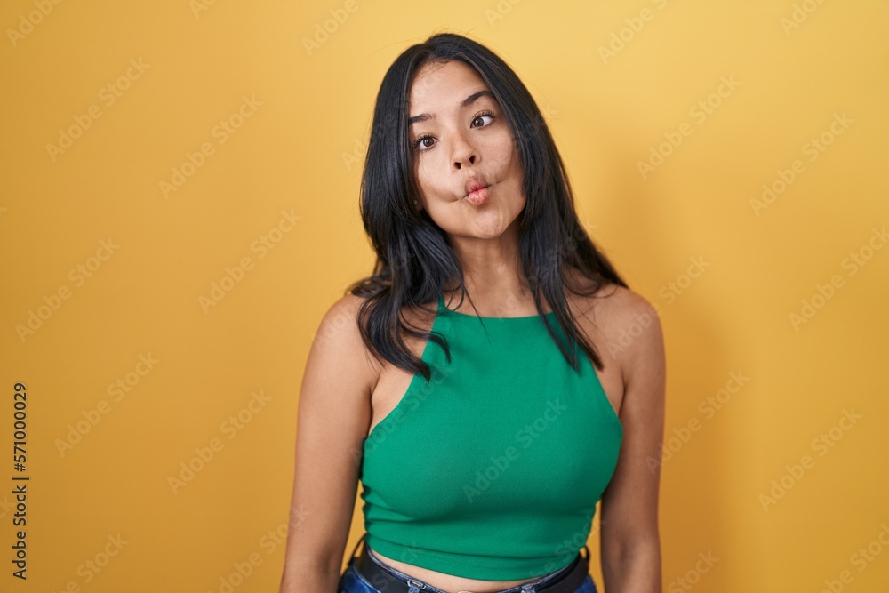 Obraz premium Brunette woman standing over yellow background making fish face with lips, crazy and comical gesture. funny expression.