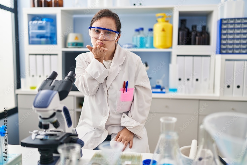 Hispanic girl with down syndrome working at scientist laboratory looking at the camera blowing a kiss with hand on air being lovely and sexy. love expression. Hispanic girl with down syndrome working at scientist laboratory looking at the camera blowing a kiss with hand on air being lovely and sexy. love expression.
