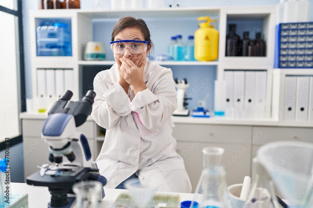 Hispanic girl with down syndrome working at scientist laboratory shocked covering mouth with hands for mistake. secret concept. Hispanic girl with down syndrome working at scientist laboratory shocked covering mouth with hands for mistake. secret concept.
