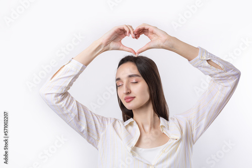Portrait of a smiling young woman showing heart gesture with her fingers isolated over white background