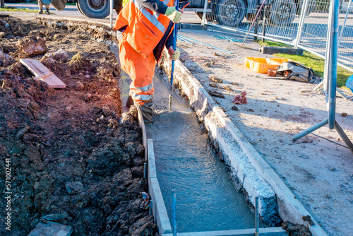 Builder pouring wall foundation with wet ready-mix concrete, levelling it and checking the level