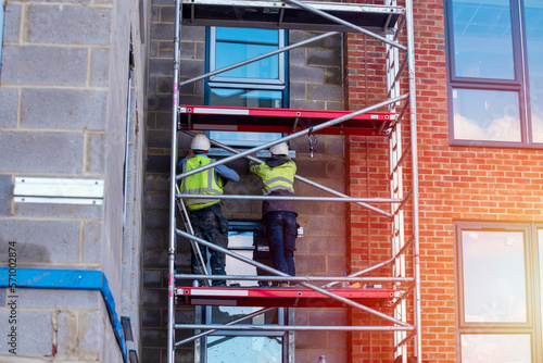 Construction workers using aluminium mobile scaffold tower and safety harness to work at height. Working at height safety regulation