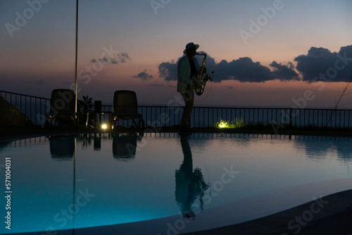 Saxophonist next a pool by sunset in tropical resort