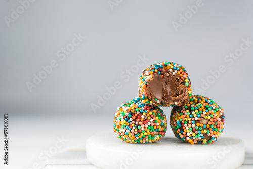 sprinkles coated chocolate truffles on a white tray, homemade chocolate bonbons covered in non pareils on white background