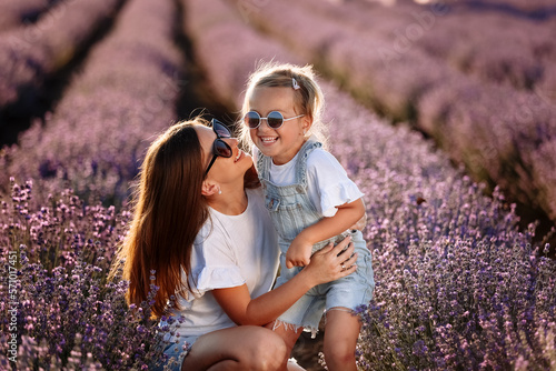 Happy family in purple lavender field. young beautiful mother and child Girl enjoy walking blooming meadow on summer day. Mom having fun with pretty daughter in nature on sunset. mothers day #571017451