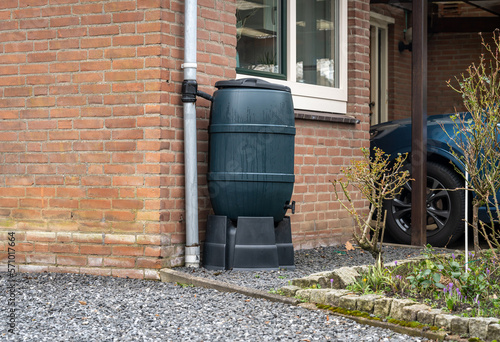 Rain barrel in front of a modern house, rainwater tank to collect rainwater and reuse it in the garden photo