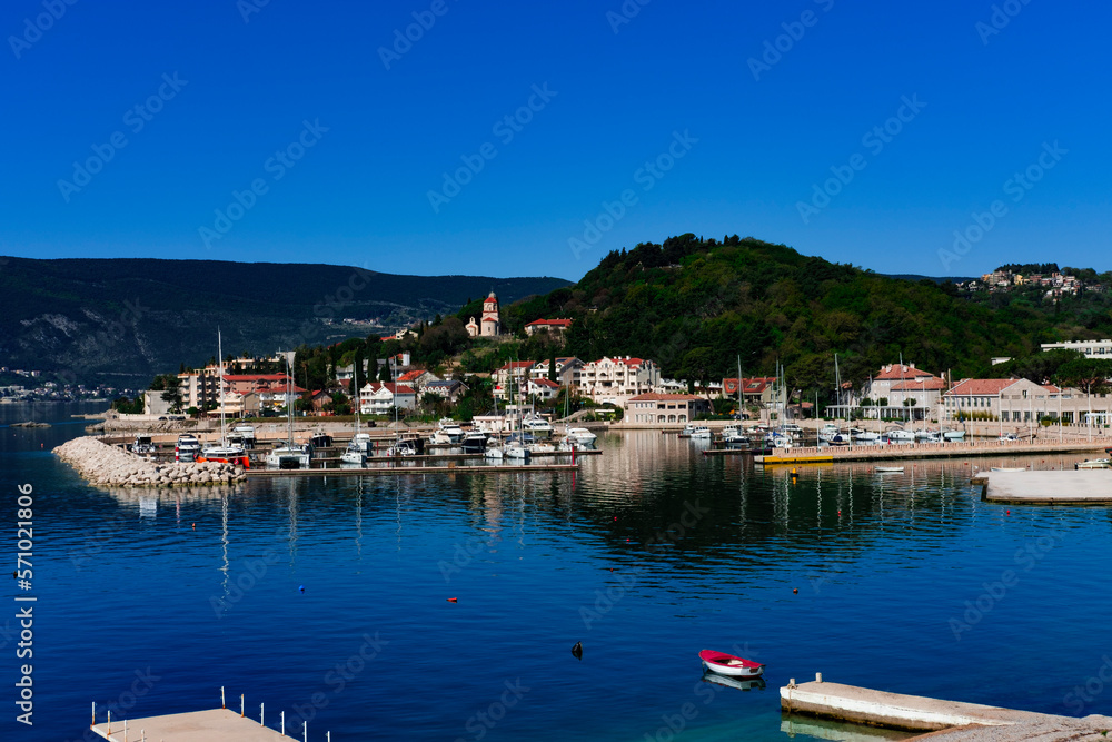 beautiful view of small adriatic town Melinje, Herceg Novi in Montenegro, green coat, stone buildings, pebble beach, fishing boats, marina with yachts at berth