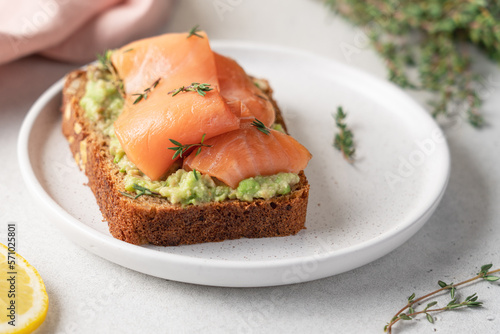 Salmon avocado sandwich on rye bread with thyme. Close-up view of fish snack. Healthy breakfast concept