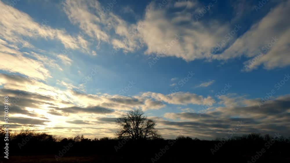 Timelapse of setting sun shining through low traveling clouds over rural landscape, with sky turning purple orange after the sun goes down Timelapse of setting sun shining through low traveling clouds over rural landscape, with sky turning purple orange after the sun goes down
