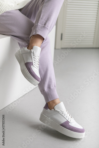 Close up trendy spring fashion outfit.female legs in lilac joggers and trendy sneakers close-up. no face