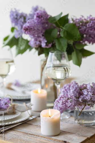 Beautiful table decor for a wedding dinner with a spring blooming lilac flowers. Celebration of a special marriage holiday event. Fancy white plates, wineglasses, candles. Countryside style